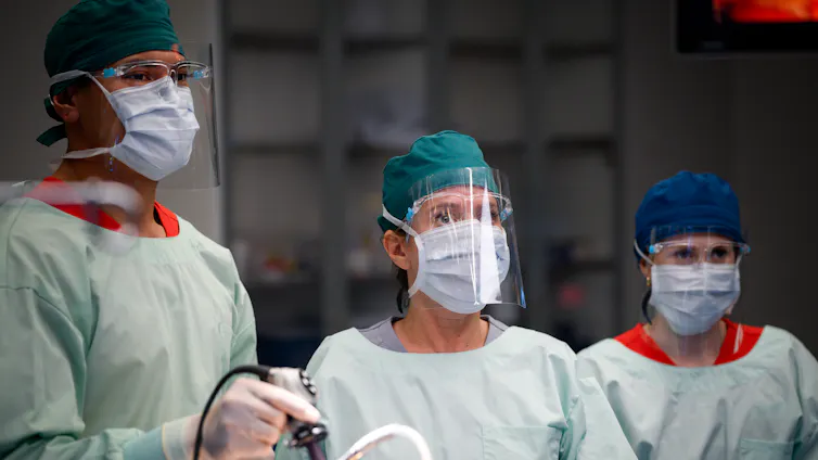 Production image: three doctors in an operating theatre.