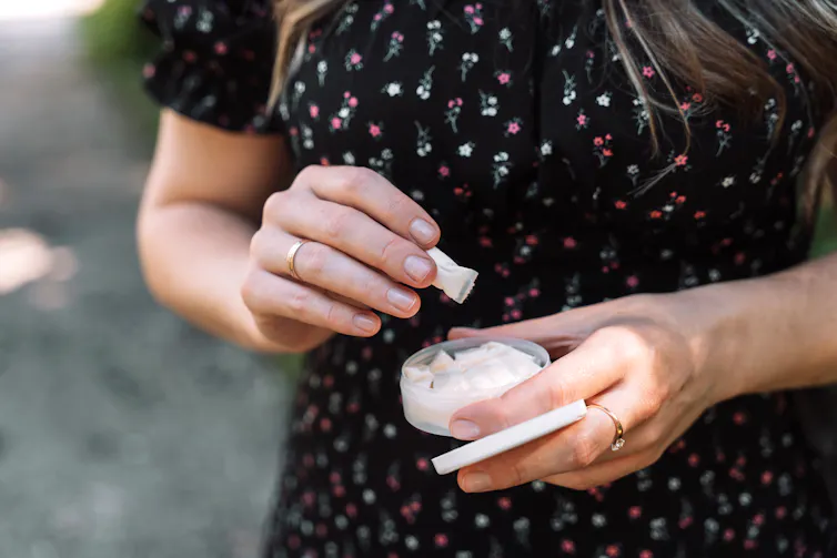 A woman takes a nicotine pouch out of a container