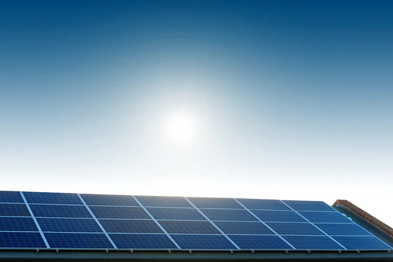 solar panels on roof and strong sun in blue sky.