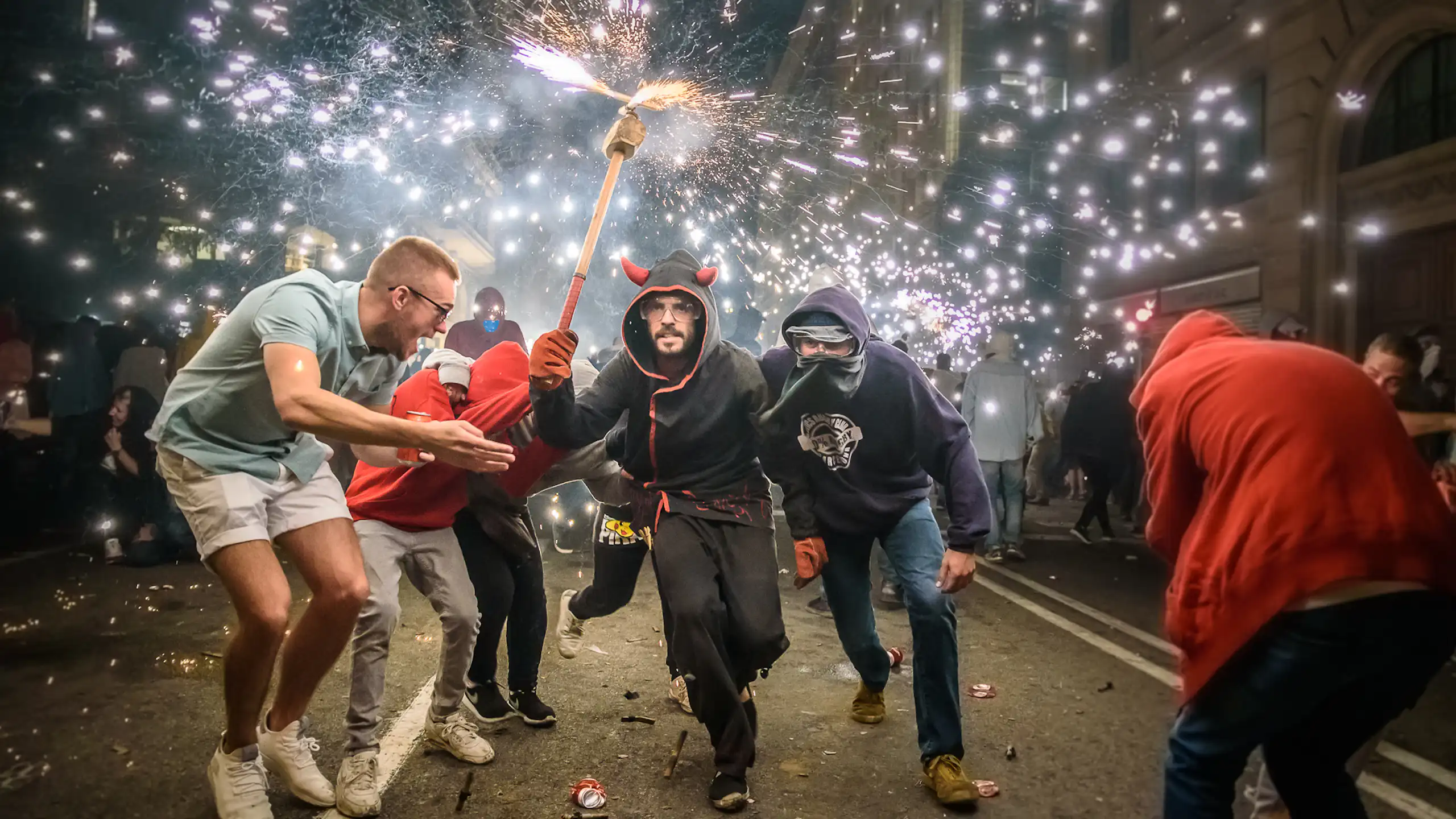 Una persona vestida de diable sostén una maça amb foc en un extrem rodejat de molta gent al carrer.