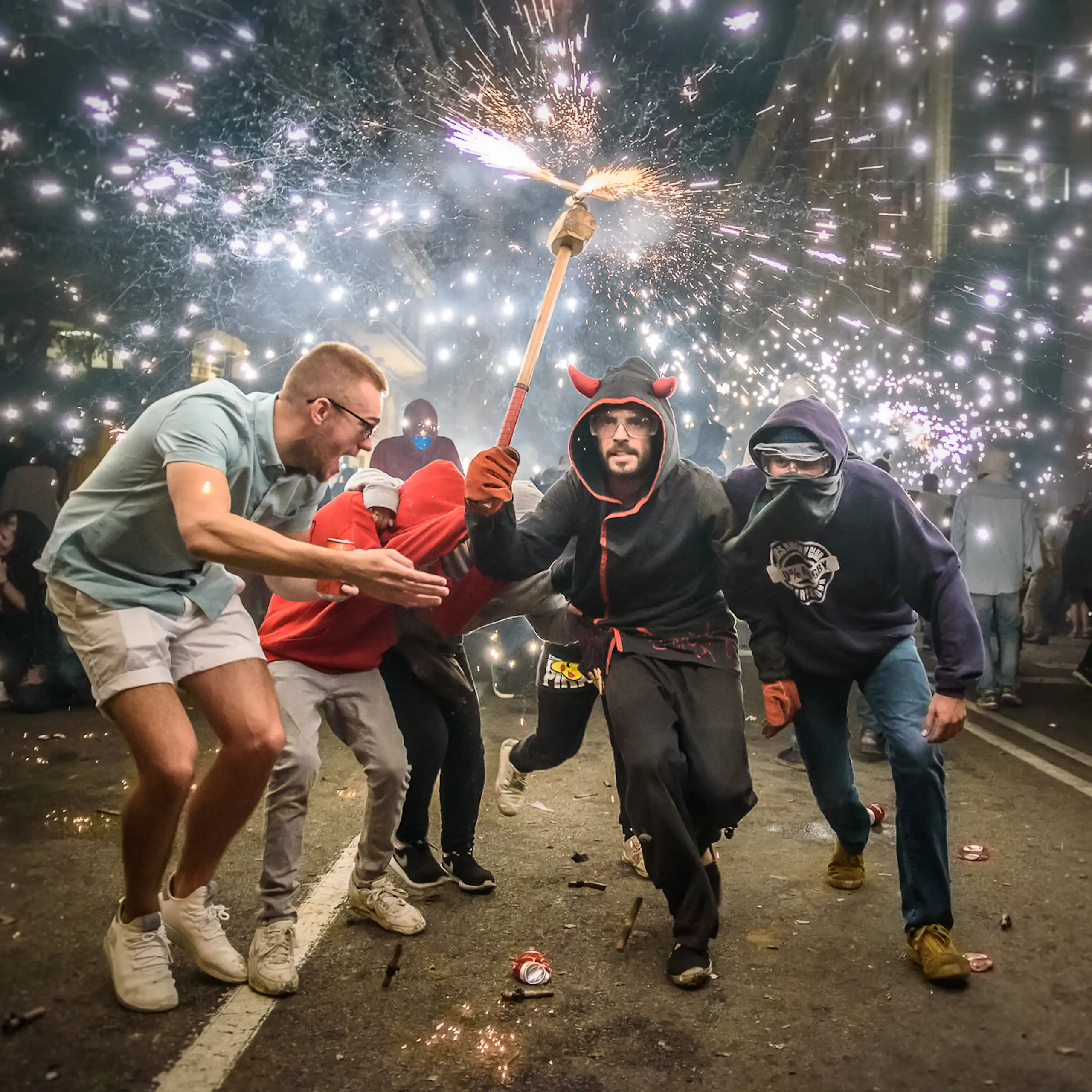 Una persona vestida de diable sostén una maça amb foc en un extrem rodejat de molta gent al carrer.