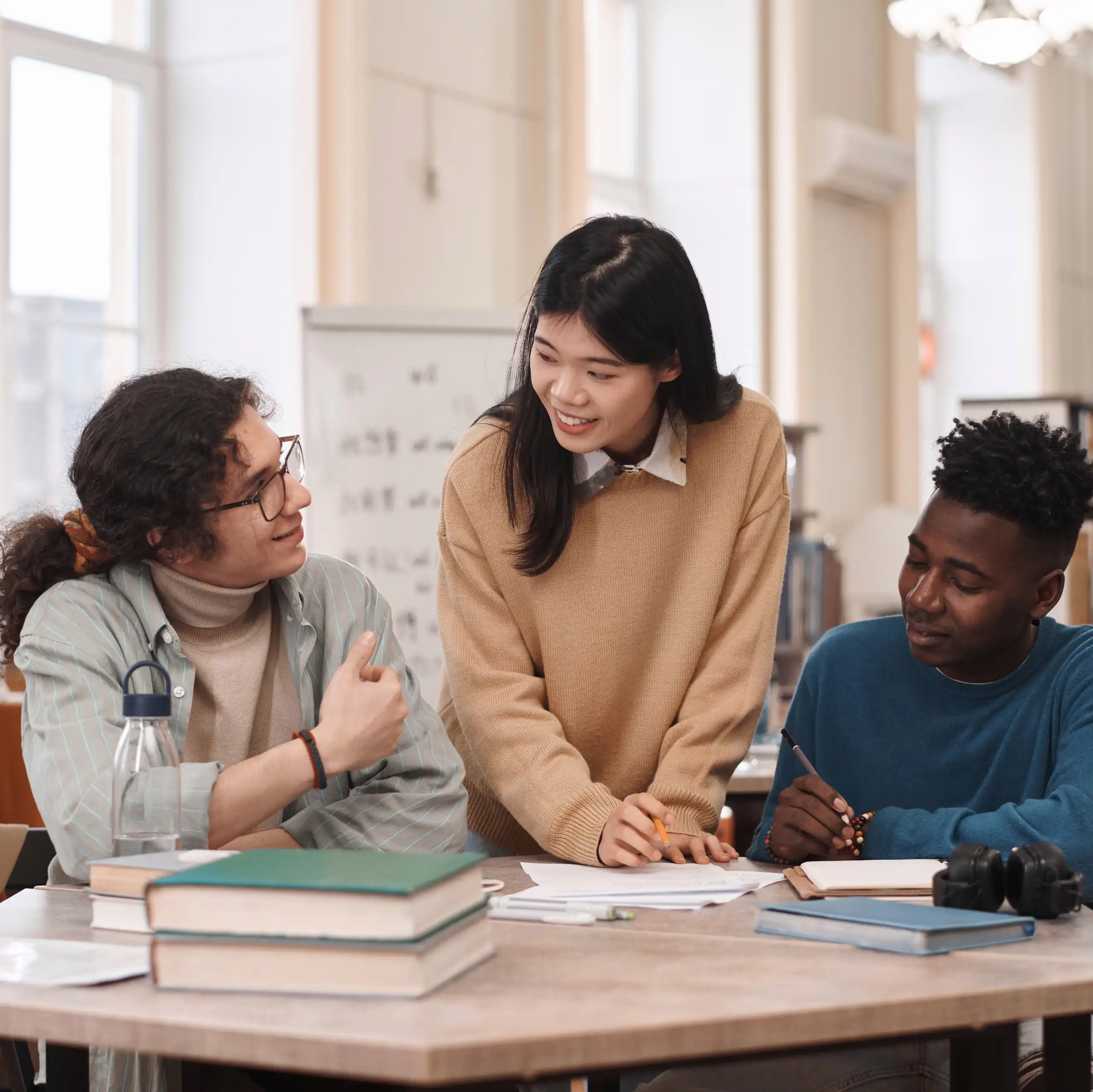 Tres estudiantes internacionales conversan en torno a una mesa con libros