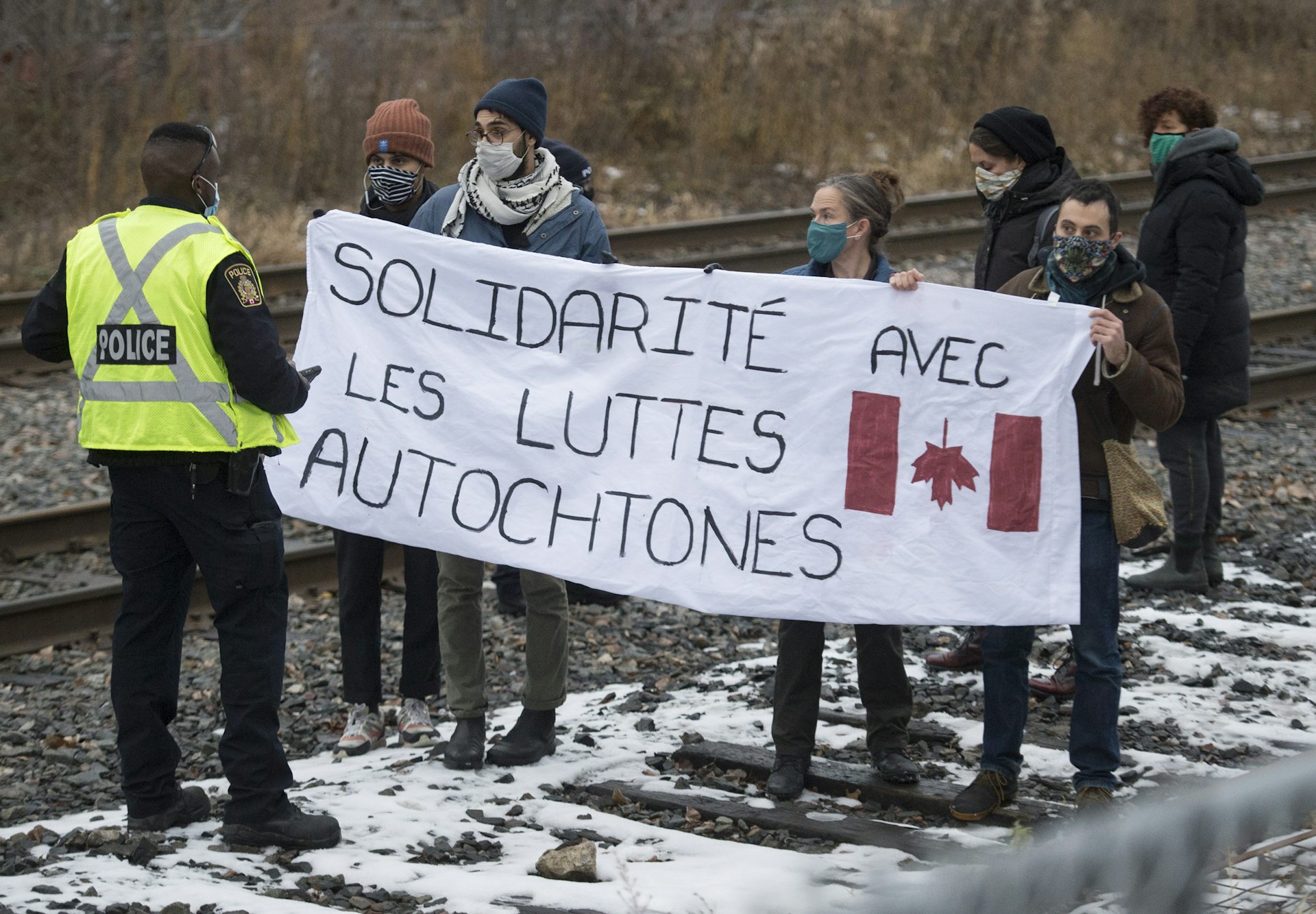 Un policier parlemente avec des manifestants qui brandissent en travers de la voie ferrée une bannière avec l’inscription « Solidarité avec les luttes autochtones. »