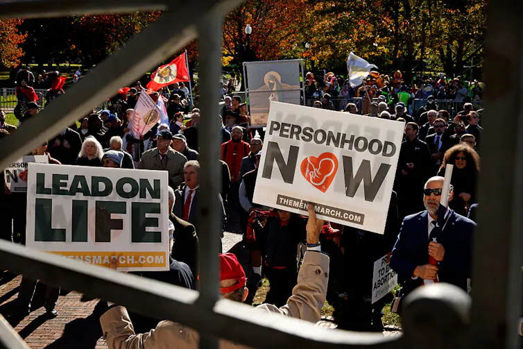 A crowd of people outside holding signs that say 'Personhood now' and 'Lead on life.'