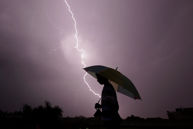 Person with an umbrella walking as lightning strikes in the background.