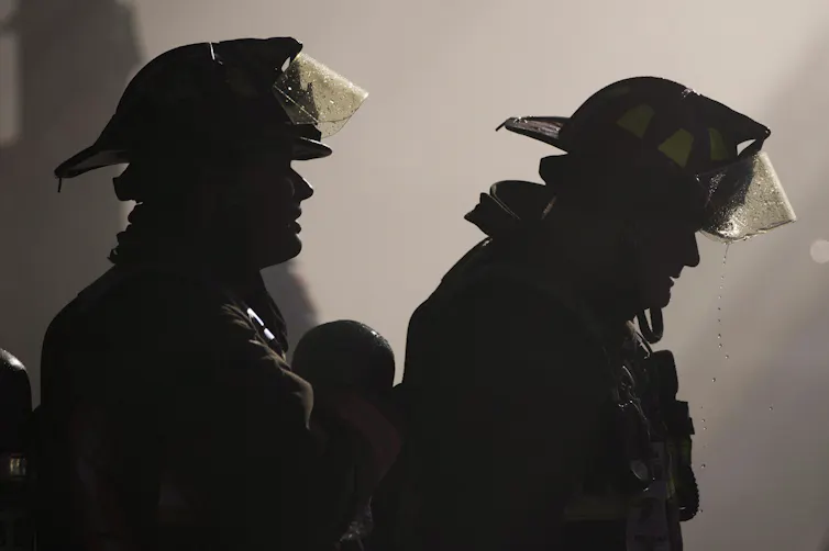 Two firefighters seen silhouetted against a smoky background