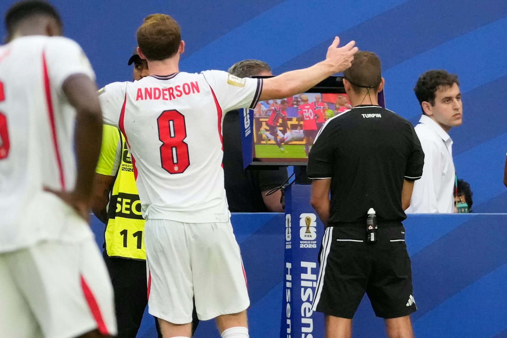 El árbitro revisa imágenes de un partido de fútbol en una pantalla mientras varios jugadores miran
