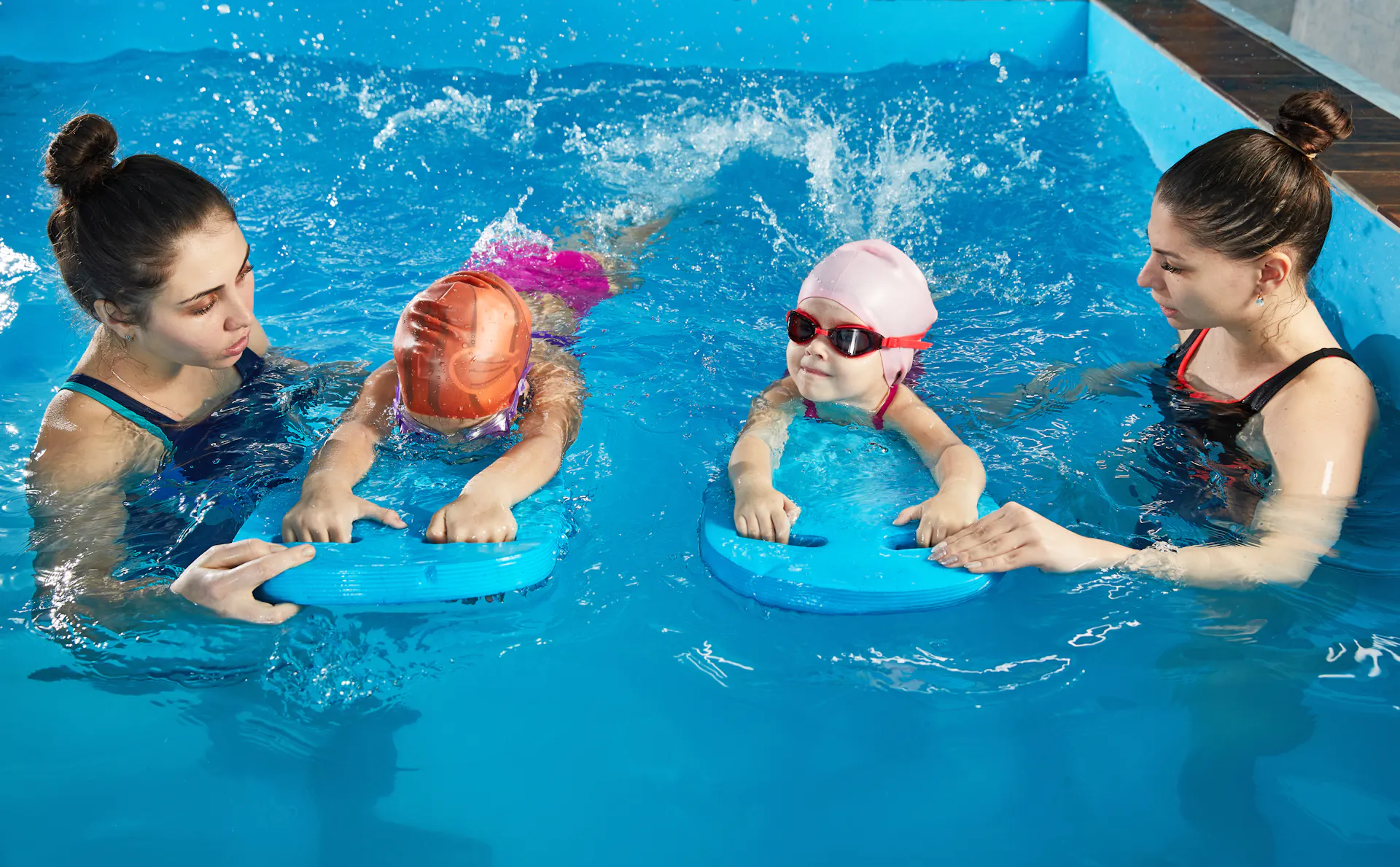 Two young children holding paddleboards work one-on-one with instructors in the pool.