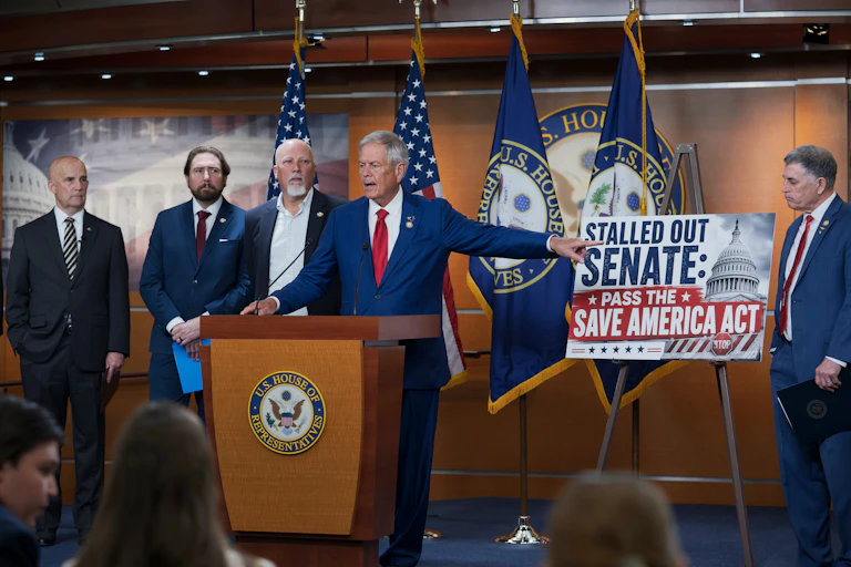 Stern men in suits stand behind a lectern, with one pointing to a sign chastising the U.S. Senate.