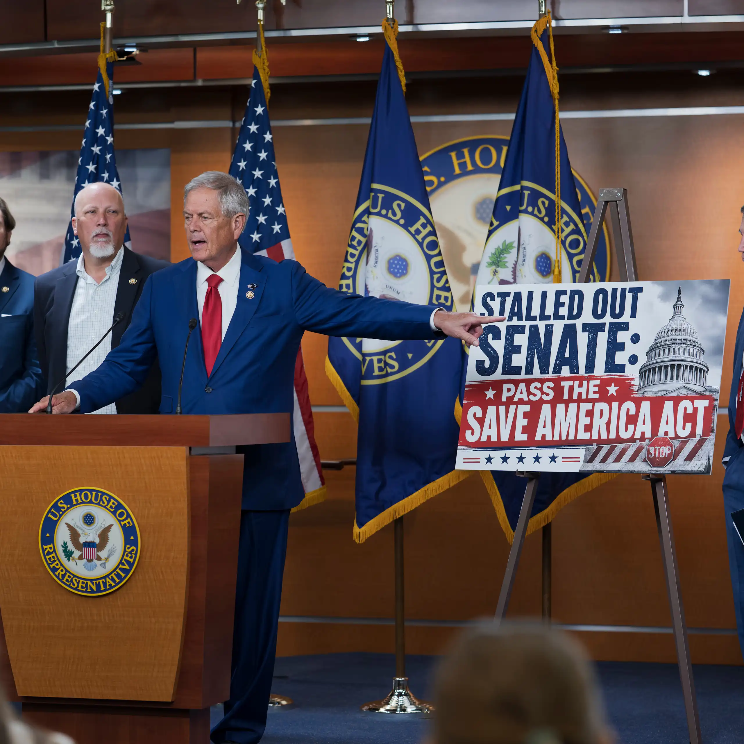 Stern men in suits stand behind a lectern, with one pointing to a sign chastising the U.S. Senate.