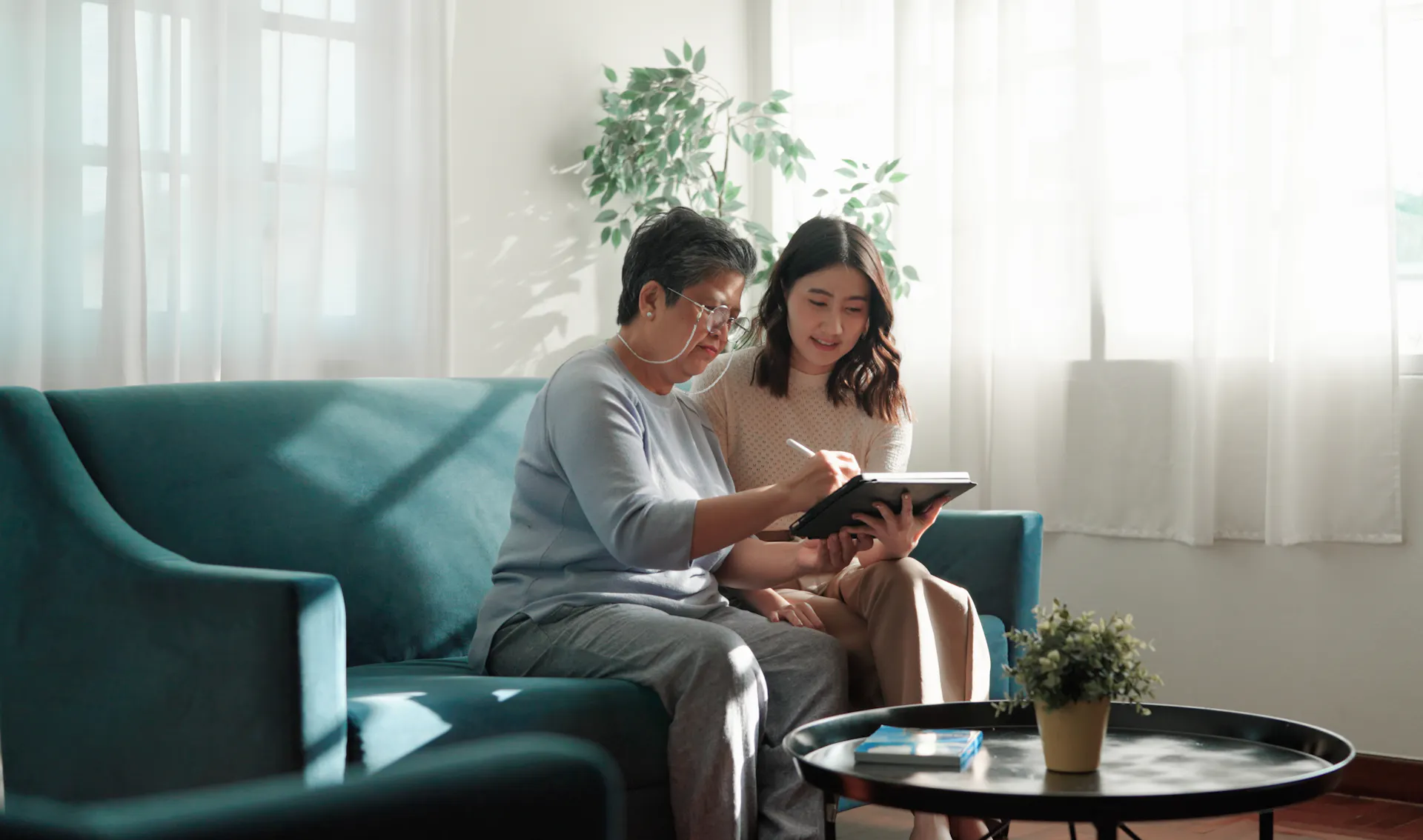 An older woman and a younger woman look at a computer screen together while sitting on a couch.