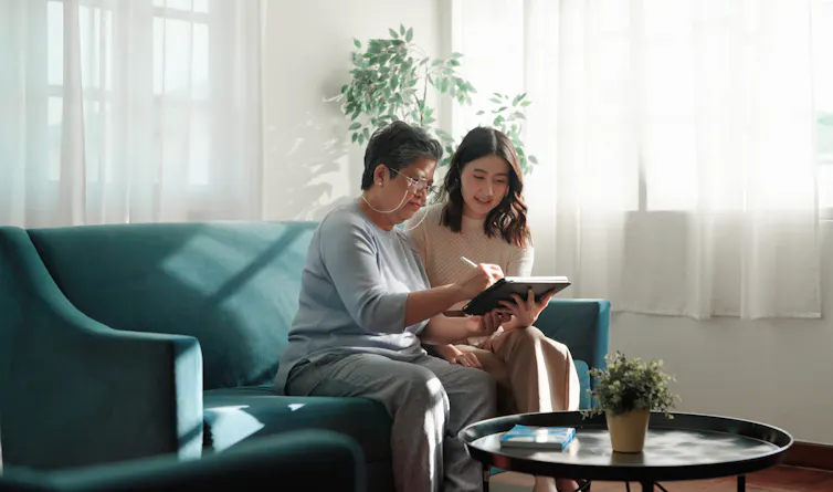 An older woman and a younger woman look at a computer screen together while sitting on a couch.