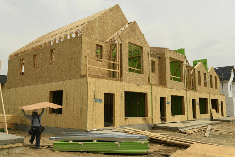Tan panels with open cut-outs for windows create the frame for a housing structure, while wood planks are on the ground at the structure's base.