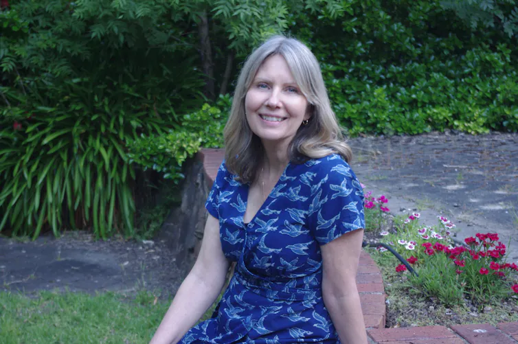 a woman in a blue dress smiling against a green garden