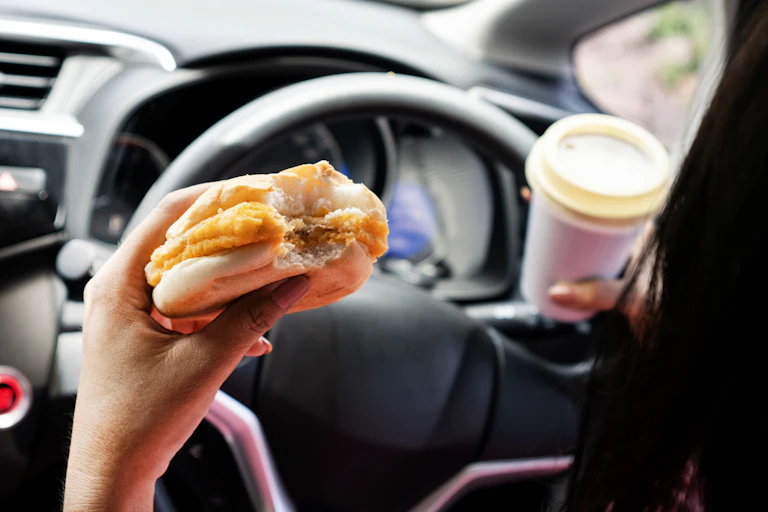 Hands holding coffee, hash brown roll and steering wheel.