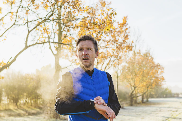 Man with frosty breath checks smart watch outside.