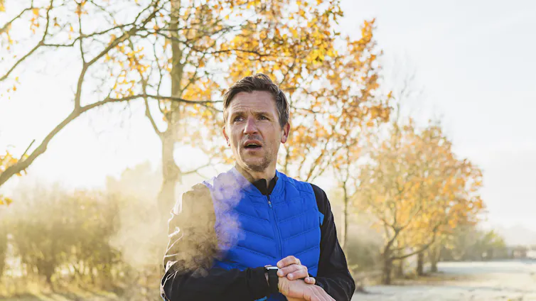 Man with frosty breath checks smart watch outside.