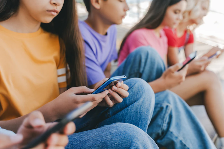 Grupo de adolescentes multirraciales sentados serios sosteniendo móviles viendo vídeos