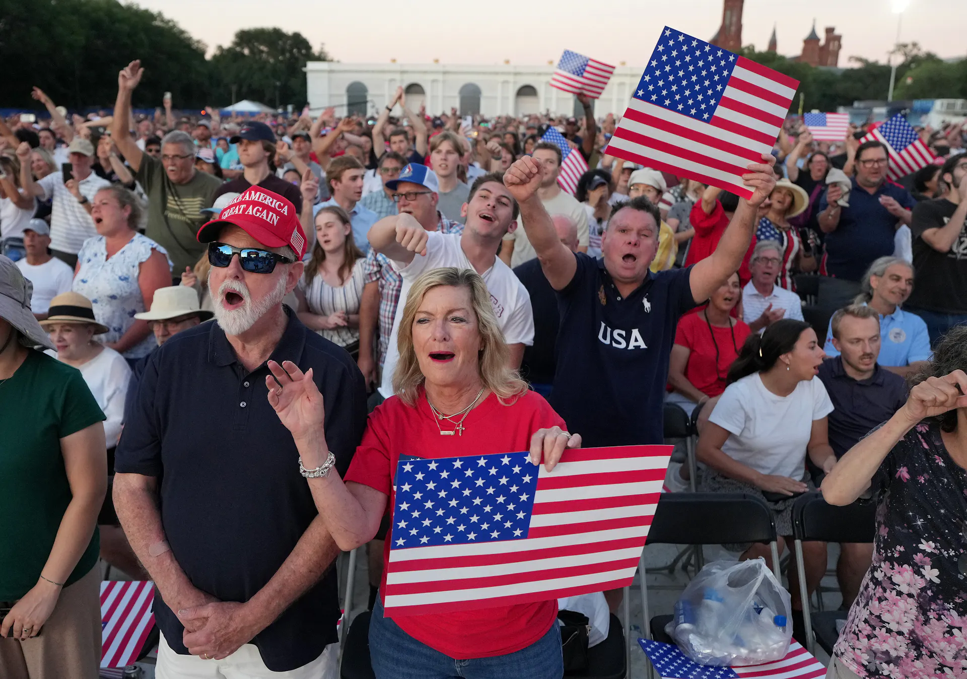 A large group of people of all ages holds U.S. flags while cheering