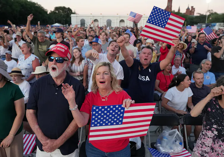 A large group of people of all ages holds U.S. flags while cheering