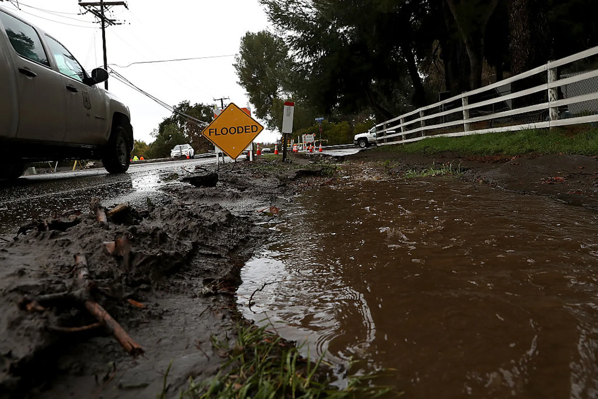 A muddy roadside ditch appears flooded with dark-hued water.