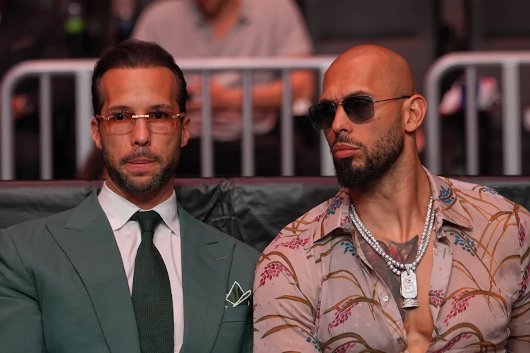 two men in sunglasses, one in suit and tie, the other in a patterned shirt
