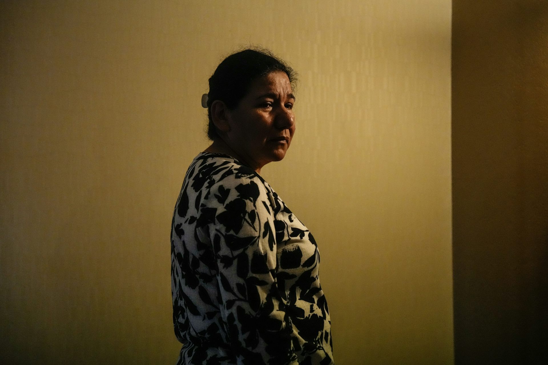 Una mujer de cabello oscuro se encuentra en el pasillo oscuro de un hotel.