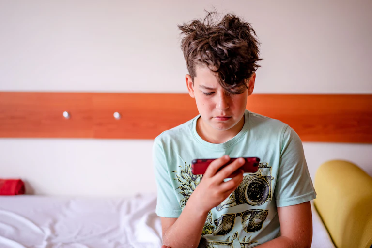 A young boy holding his phone, looking sad and worried.