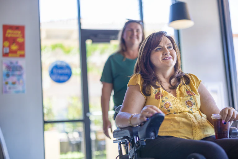 A disabled woman enters a shop with her support worker
