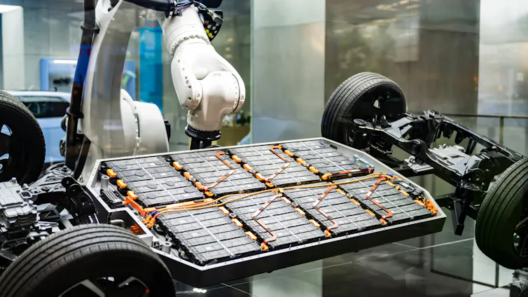 electric car being built by robot arms in factory. battery array showing.