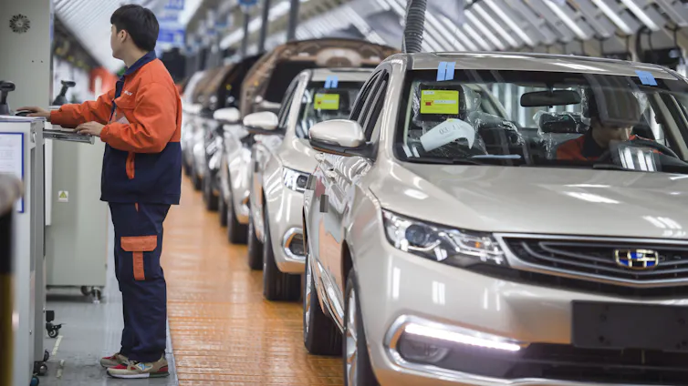 A worker stands next to a car factory assembly line.