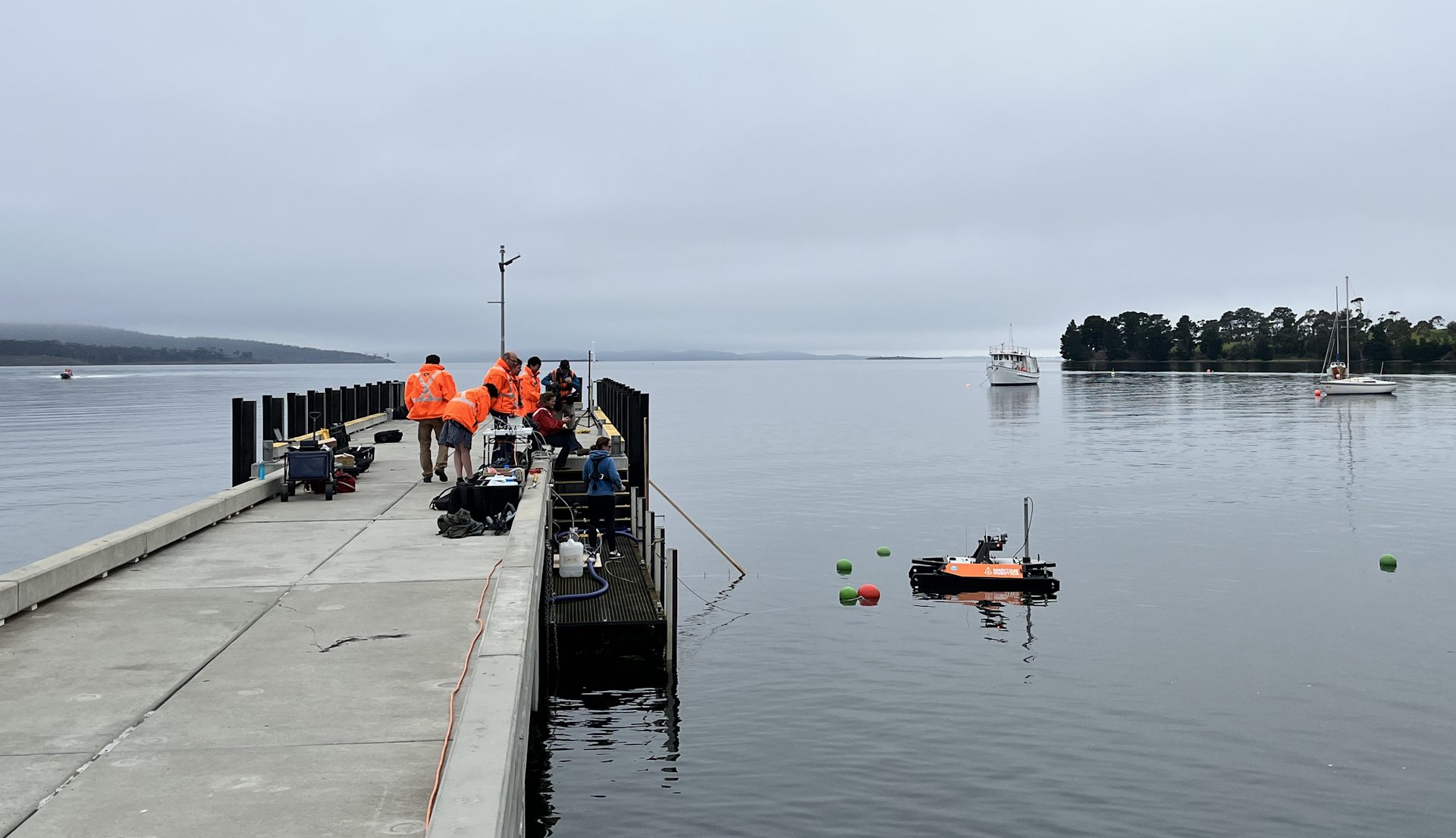 A group of researcheit ours in orange jackets on a jetty, conducting field tests.