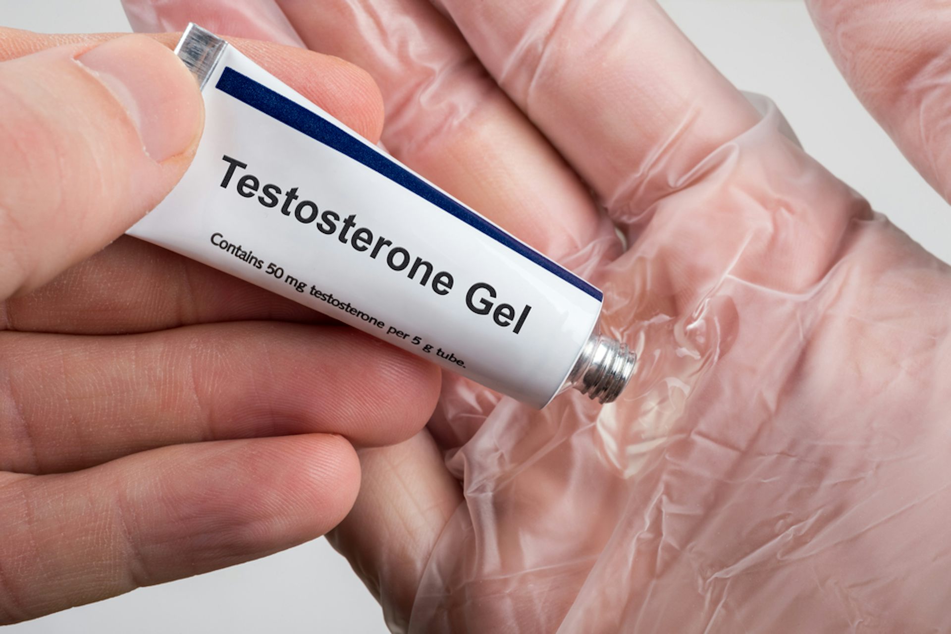 A man squeezing testosterone gel onto a glove hand before applying it.