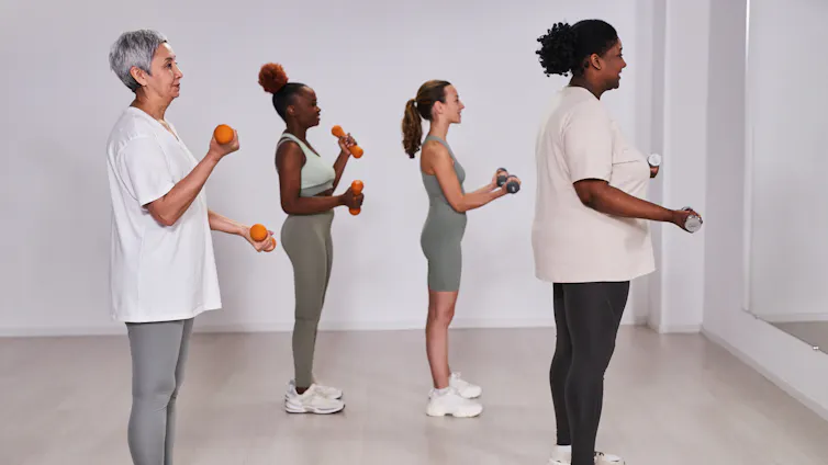 A group of four women of different ages perform bicep curls using dumbbells.