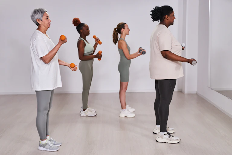 A group of four women of different ages perform bicep curls using dumbbells.
