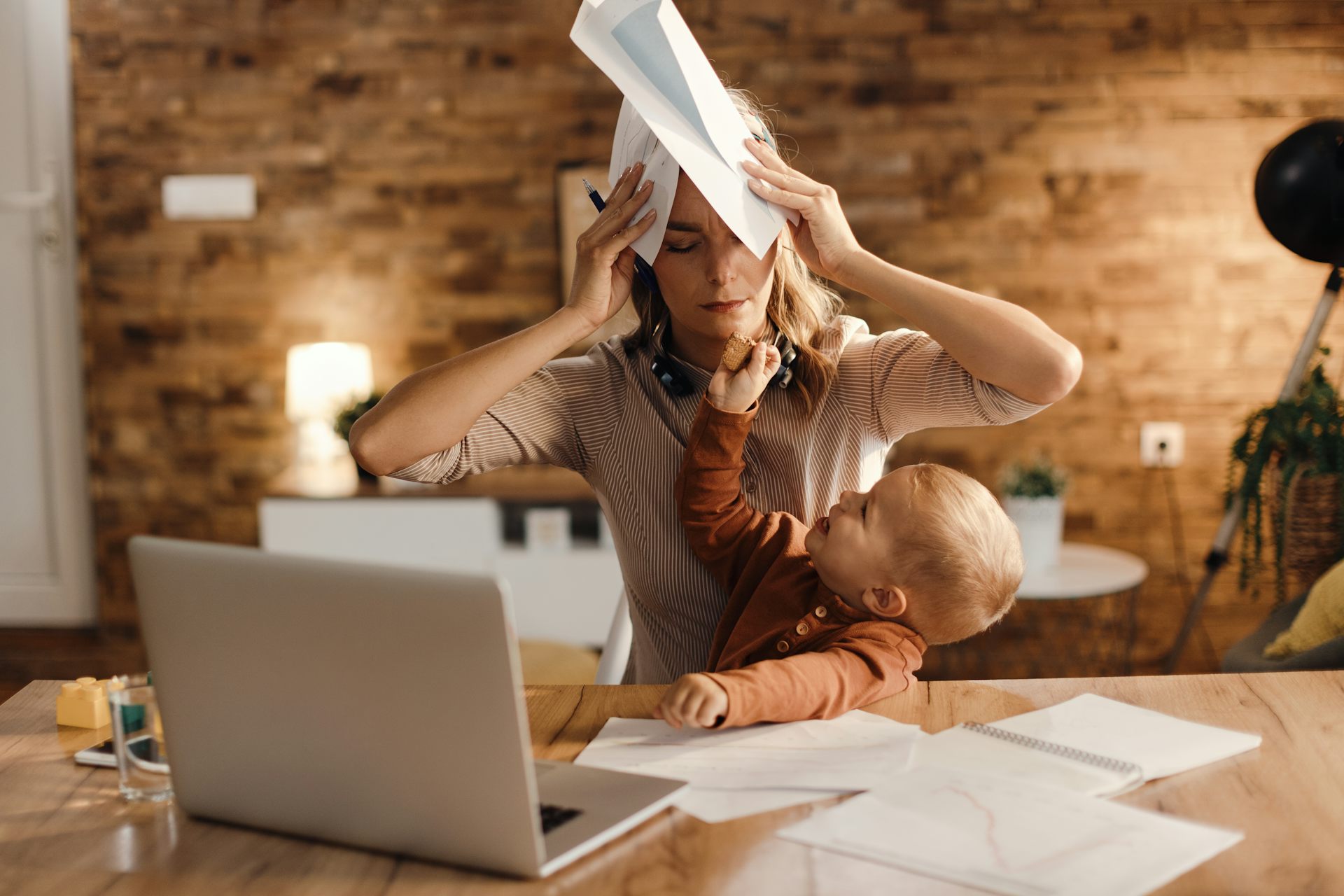A woman appears stressed while trying to work at home with a toddler on her lap