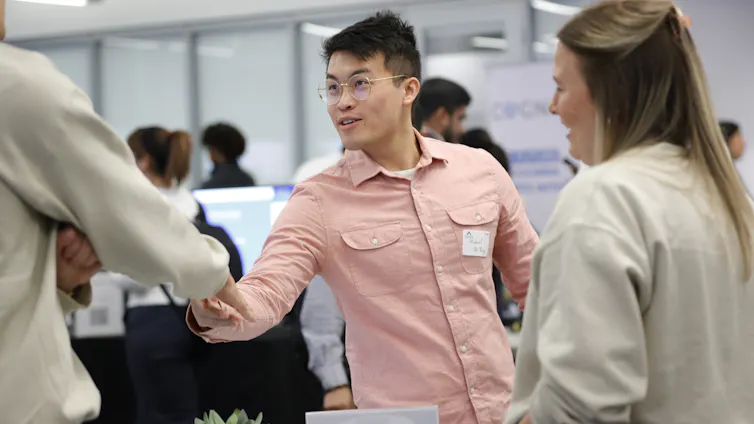 A Georgia Tech student in a light coral shirt, Michael Oh-Yang, shakes hands with company representatives at a job fair in Atlanta.