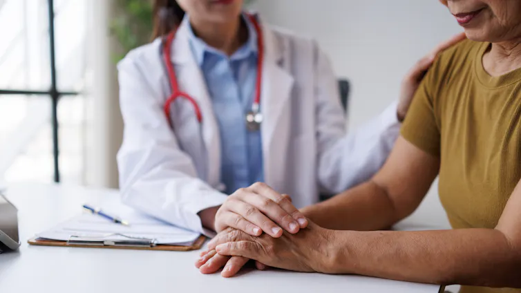 Una médica posa sus manos sobre las de una paciente mayor
