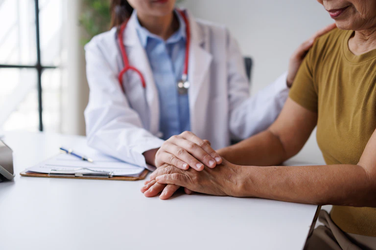 Una médica posa sus manos sobre las de una paciente mayor