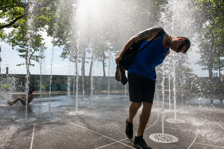 Por qué 78 grados no es la configuración adecuada del termostato para todos durante una ola de calor 1 Un hombre sumerge la cabeza en el chorro de agua que brota de una fuente en el suelo.