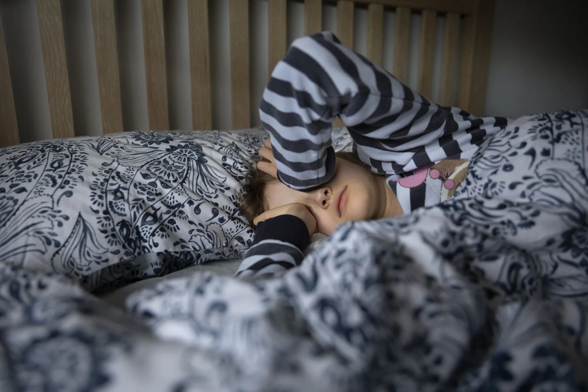 Child lying in bed rubbing their eyes upon waking up