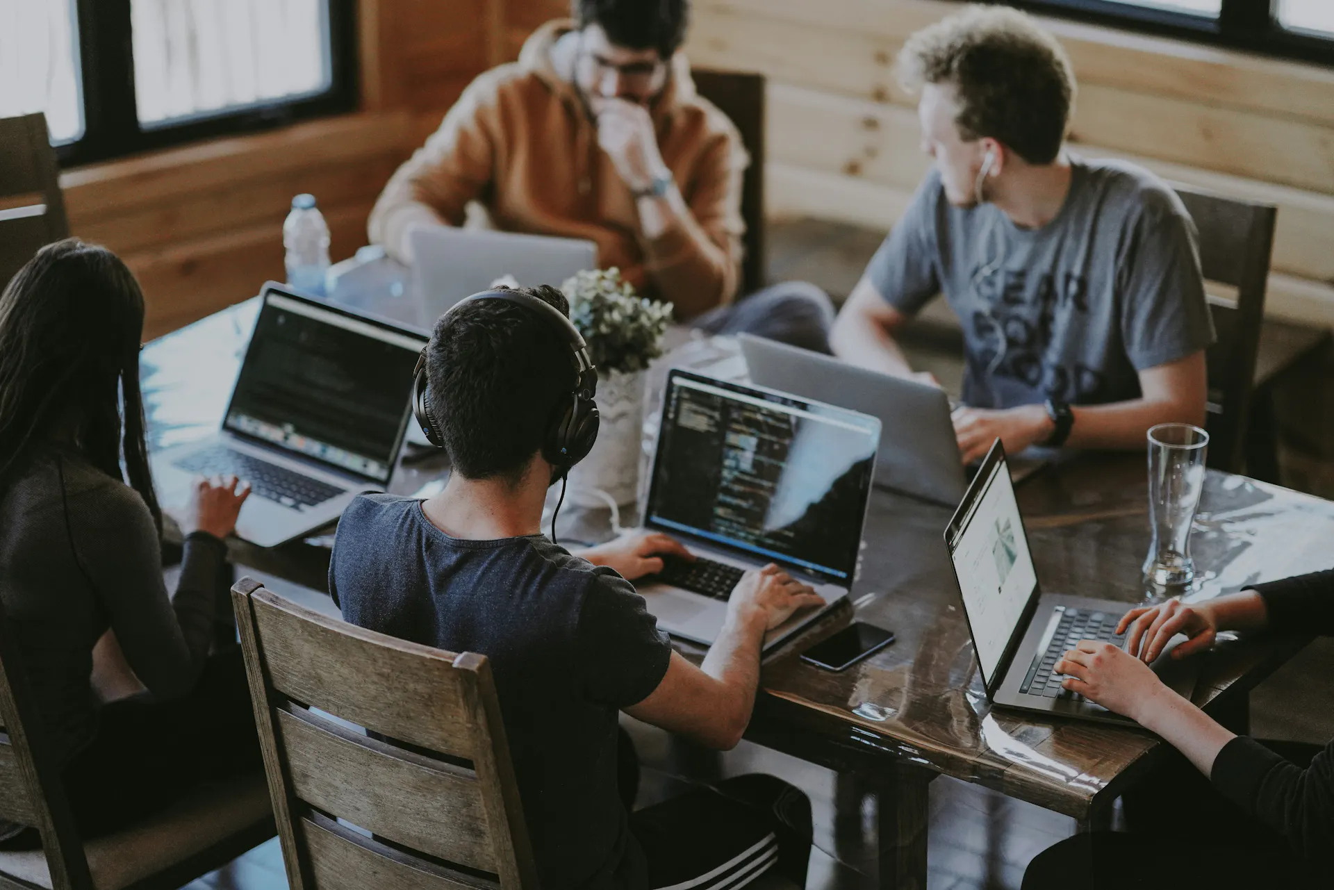Five people with laptops sit at a table, talking with each other.