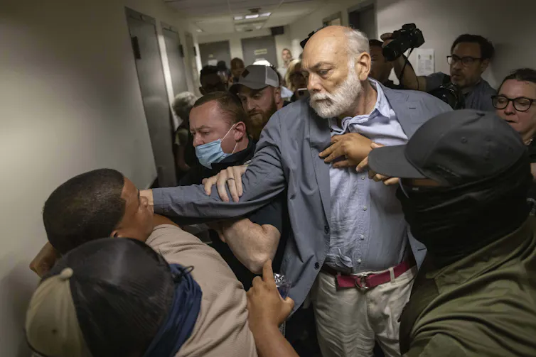 A medida que se expande la red de vigilancia y la red de control tecnológica de ICE, los activistas están lidiando con sus propios datos 1 Un grupo de personas peleando con agentes de ICE en el juzgado.