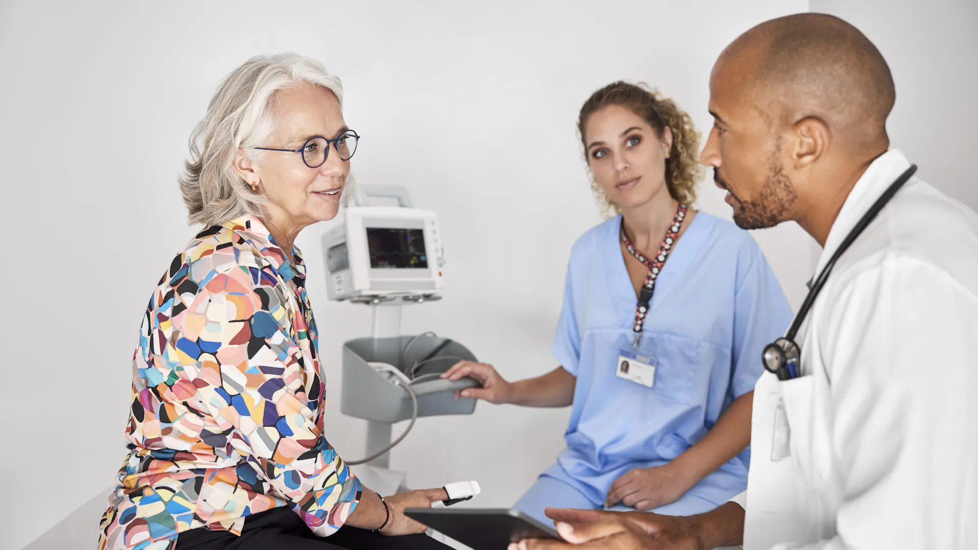 A female patient sits on an exam table, talking with a doctor and nurse