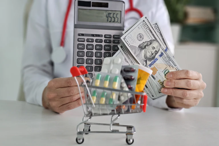 The headless torso of a doctor, wearing a stethoscope around their neck and holding a calculator in one hand and a stack of $100 bills, with a tiny shopping cart full of pills sitting in front of them