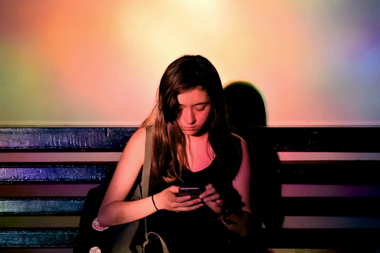 A woman gazes at her phone, her long hair faling over her face, in moody lighting.