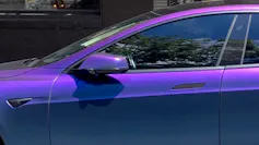 A purple Tesla with its electric handle retracted into the door.