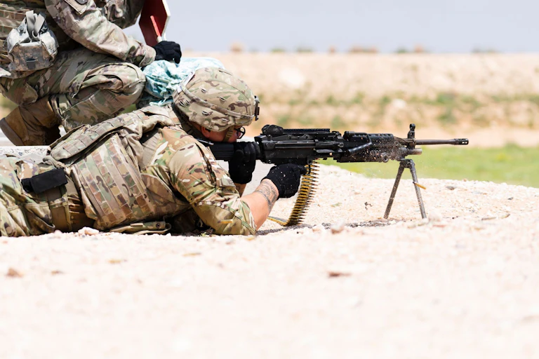 US soldier lying on ground, holding rifle, taking aim at distant target