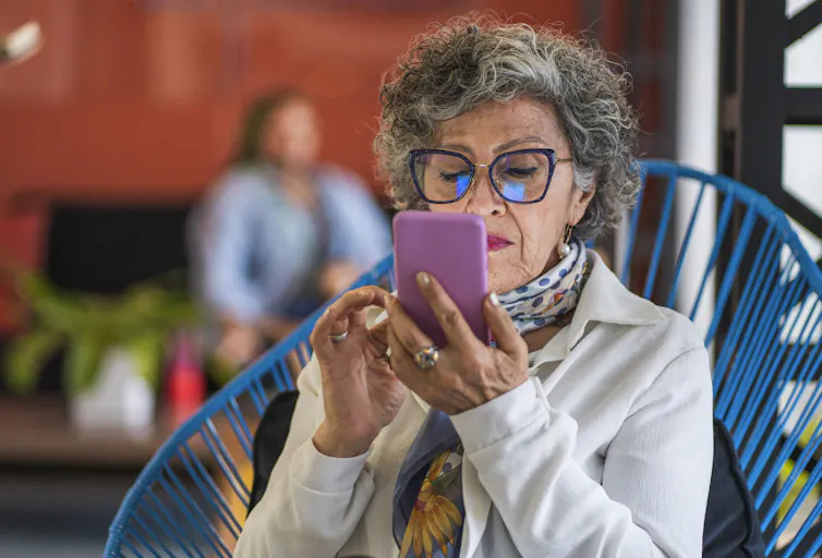 An older woman in a fabulous outfit reads something on her purple smartphone.