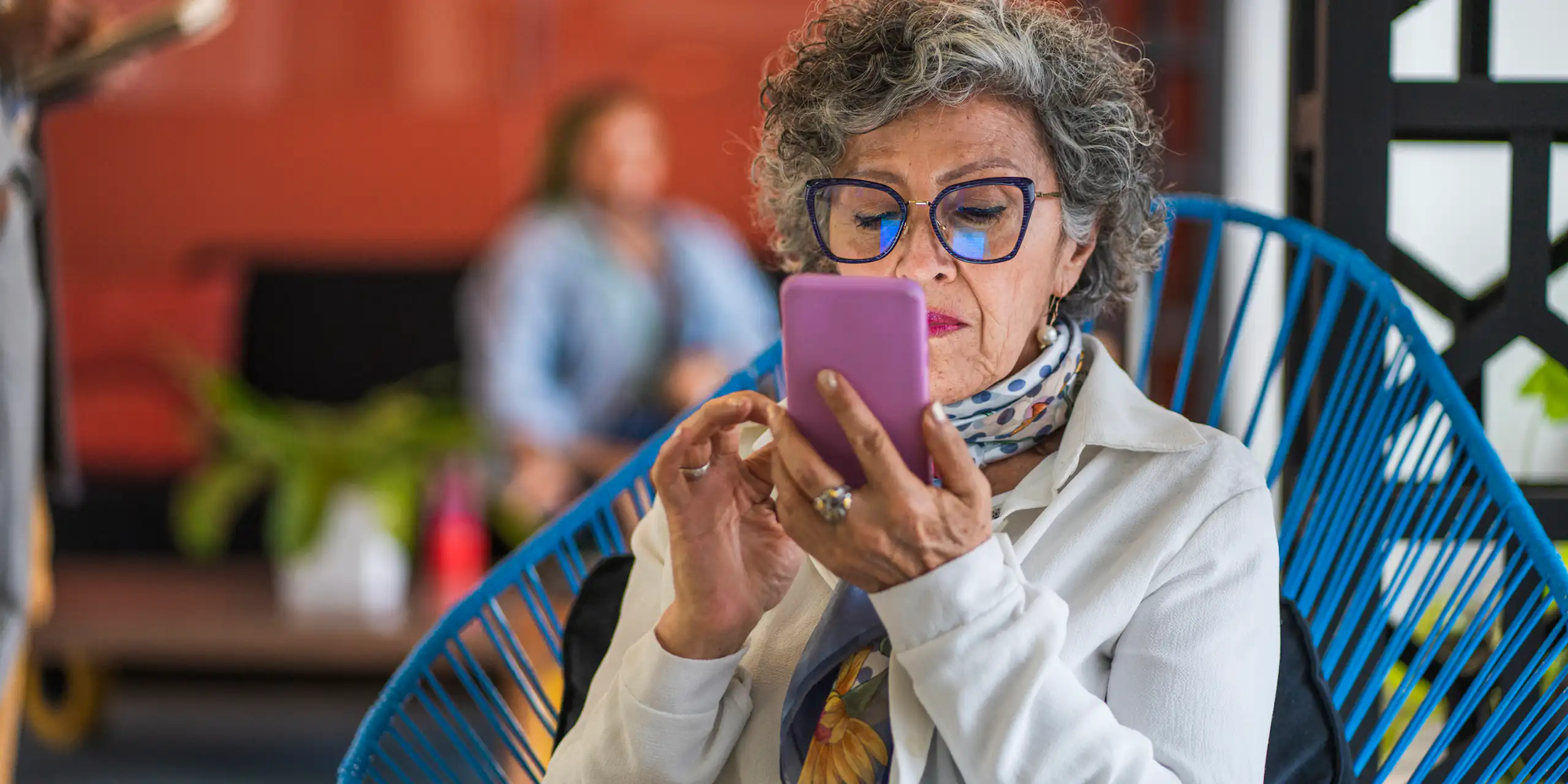 An older woman in a fabulous outfit reads something on her purple smartphone.